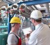 Arbeiter mit Schutzhelmen in Industrieanlage inspizieren einen tragbaren Bildschirm