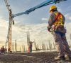 A construction worker control a pouring concrete pump on construction site and sunset background