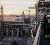 Eine Raffinerie bei Sonnenuntergang rechts im Bild zwei Arbeiter